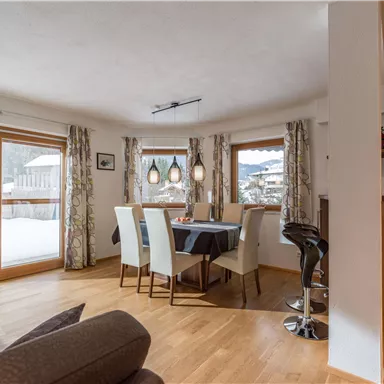 Ein helles Esszimmer mit einem Tisch und Stühlen. Große Fenster lassen viel Licht herein und bieten einen Blick auf die winterliche Landschaft.