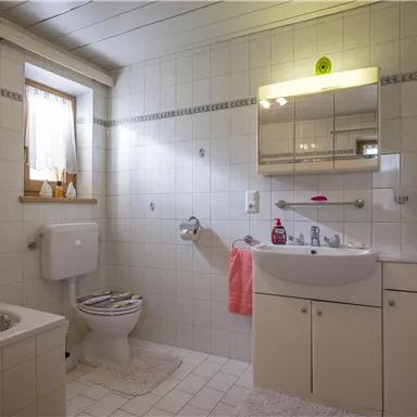 Ein helles Badezimmer mit weißen Fliesen und einem großen Spiegel. Es gibt eine Badewanne, ein Waschbecken und einen WC-Bereich.