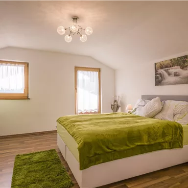 Ein modernes Schlafzimmer mit einem großen Bett und grüner Bettwäsche. Die Einrichtung umfasst einen Schreibtisch und eine gemütliche Atmosphäre.