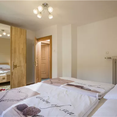 Ein modernes Schlafzimmer mit zwei Betten und einem großen Spiegel. Das Zimmer hat eine ruhige Atmosphäre und warmes Licht.