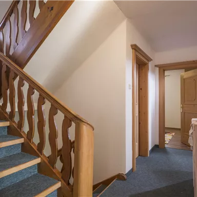 Ein treppenhaus mit Holzgeländer und blauen Teppichboden. Es gibt mehrere Türen, die zu verschiedenen Räumen führen.