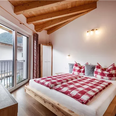 A cozy bedroom with a large bed and checkered bedspreads. Bright walls and a wooden ceiling create an inviting atmosphere.