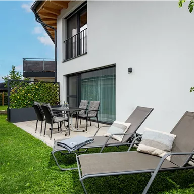 A modern garden area with two loungers and a dining table. The building is bright and invites relaxation.