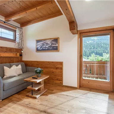 Ein gemütlicher Raum mit Holzverkleidung, einem Sofa und einem kleinen Tisch. Große Fenster bieten einen Blick auf die Natur draußen.