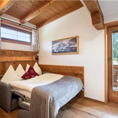 Ein gemütliches Schlafzimmer mit Holzdetails und einem Doppelbett. Ein Fenster bietet einen Blick auf die Berge und den Garten.