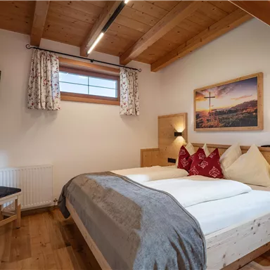 Ein gemütliches Schlafzimmer mit zwei Betten, Holzdetails und einem Fernseher. Große Fenster lassen viel Licht herein und bieten eine angenehme Atmosphäre.