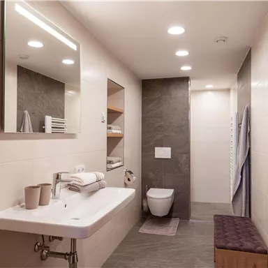 Ein modernes Badezimmer mit einer eleganten Waschbecken-Einheit und einer stilvollen Dusche. Die Wände sind hell und die Einrichtung ist schlicht und funktional.