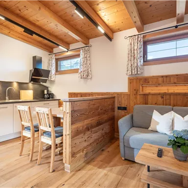 Gemütlicher Wohnraum mit einer offenen Küche und Holzmöbeln. Der Raum ist hell und einladend, mit natürlichem Licht durch die Fenster.