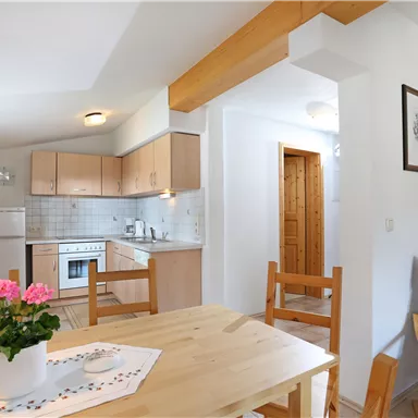 A bright living and dining room with a modern kitchen. The table is decorated with a flower and there is a blue armchair.