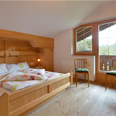 Ein gemütliches Schlafzimmer mit Holzdekor und einem großen Fenster. Es gibt ein Doppelbett und zwei Stühle, die eine einladende Atmosphäre schaffen.