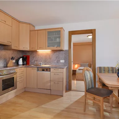 Eine moderne Küche mit Holzmöbeln und Geräten. Daneben steht ein Esstisch mit Stühlen in einem gemütlichen Raum.