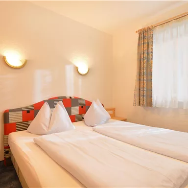 Ein gemütliches Schlafzimmer mit zwei Einzelbetten und heller Bettwäsche. Der Raum hat Fenster mit Vorhängen und sanfte Wandleuchten.