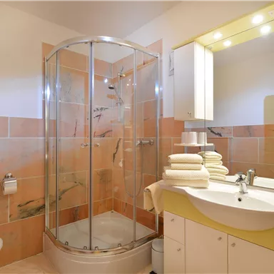 Ein modernes Badezimmer mit einer Duschkabine und einer hellen, freundlichen Farbgestaltung. Saubere Handtücher liegen auf dem Waschbecken bereit.