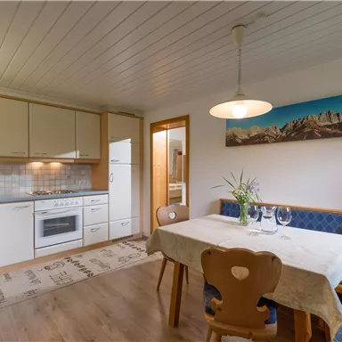 Ein gemütlicher Essbereich mit einer modernen Küche. Der Tisch ist schön gedeckt und es gibt eine große Fensterfront mit Blick auf die Berge.