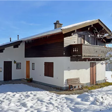 A traditional house in Alpine style, surrounded by snow. The clear blue sky creates a peaceful winter atmosphere.
