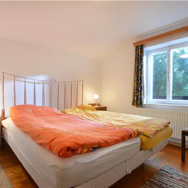 Ein gemütliches Schlafzimmer mit einem Doppelbett und bunten Bettwaren. Das Zimmer hat ein Fenster mit Vorhängen und einen kleinen Nachttisch.