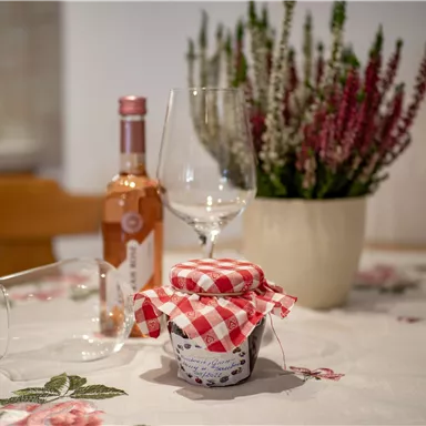 A cozy table with a glass and a bottle of rosé wine. In the center is a glass with a checked lid and a blooming plant.