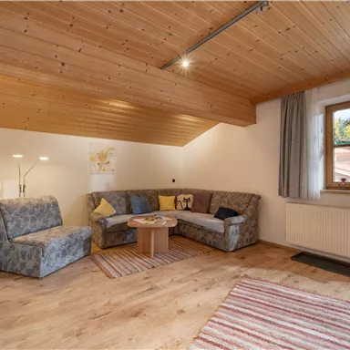 A cozy living room with a modern couch and a wooden table. Large windows let in plenty of light and create an inviting atmosphere.
