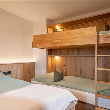 Ein helles Zimmer mit zwei Betten, darunter ein Hochbett aus Holz. Die Wände sind mit warmem Holz verkleidet, und die Bettwäsche ist in sanften Farben gehalten.