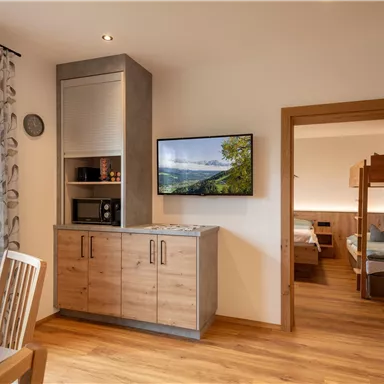 Eine moderne Küche mit Holzinterieur und einem Fernseher an der Wand. Im Hintergrund ist ein Schlafzimmer sichtbar.