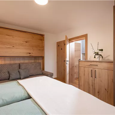 Ein modernes Schlafzimmer mit hellem Holzinterieur. Es gibt ein Doppelbett, ein Sofa und einen Kleiderschrank.