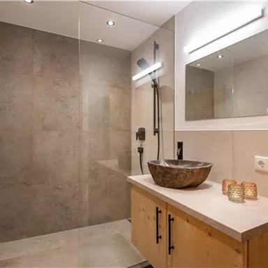 Ein modernes Badezimmer mit einer Walk-in-Dusche und stilvollem Waschbecken. Handtücher in sanften Farben sind ordentlich gestapelt.