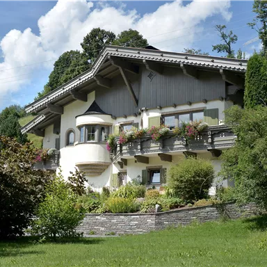 A cozy house with balconies and colorful flowers. Surrounded by green grass and trees under a clear sky.