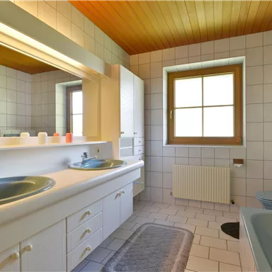 A bright bathroom with two sinks and large mirrors. The white tiles and wooden ceiling create a bright, friendly atmosphere.