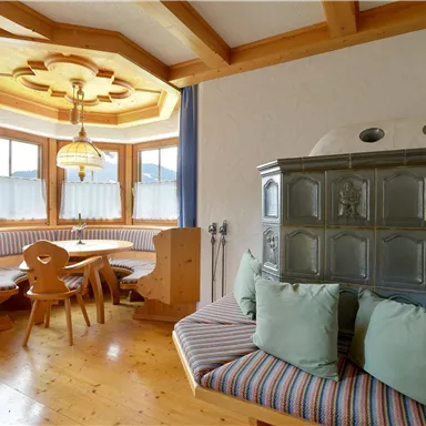 A cozy dining area with a wood stove and a round table. The windows let in plenty of light, and the room has a warm, inviting atmosphere.