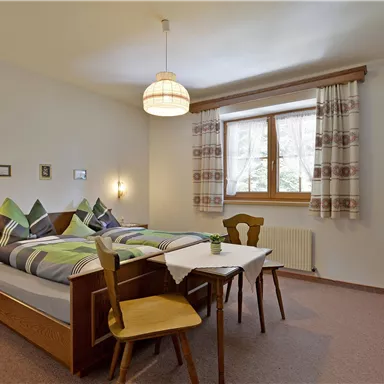 A cozy bedroom with a double bed and wood-colored furniture. Bright atmosphere with a window and soft curtains.