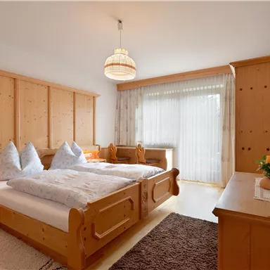 A cozy bedroom with wooden paneling and two beds. The room has large windows with plenty of natural light.