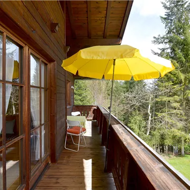 A cozy balcony with a yellow sunshade and wooden railing. In the background, there are trees and a green meadow.