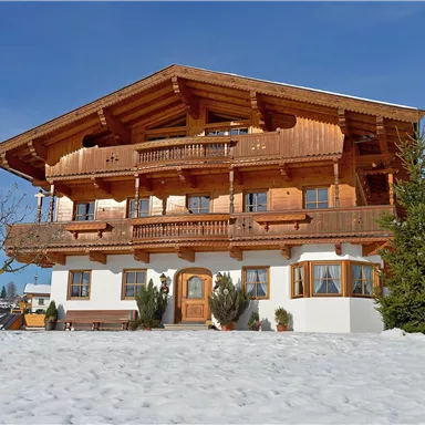 Ein traditionelles Holzhaus in den Bergen, umgeben von Schnee. Der klare blaue Himmel ergänzt die malerische Winterlandschaft.