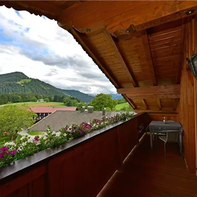 A beautiful balcony with wooden walls and flower boxes. In the background, green mountains and an idyllic landscape can be seen.