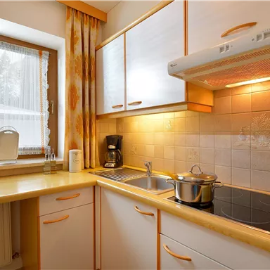 Eine moderne Küche mit hellen Schränken und einem Fenster. Auf der Arbeitsplatte steht ein Topf und eine Kaffeemaschine.