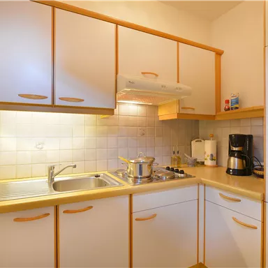 Eine moderne Küche mit hellen Schränken und einer Arbeitsfläche. Auf der Theke sind ein Topf und eine Kaffeemaschine zu sehen.