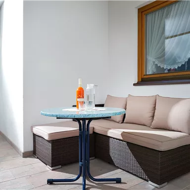 Ein gemütlicher Balkon mit einem runden Tisch und einer Couch. Auf dem Tisch stehen Getränke, um eine entspannte Atmosphäre zu schaffen.