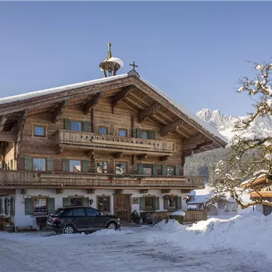 Ein rustikales Holzhaus im Winter, umgeben von Schnee. Der Himmel ist klar und die Landschaft wirkt friedlich.