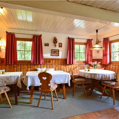 A cozy restaurant with wooden paneling and warm colors. The tables are set and there are windows with curtains that let in plenty of light.