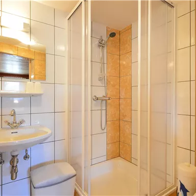 A modern bathroom with a glass shower and a sink. The walls are brightly tiled and there are practical shelves.