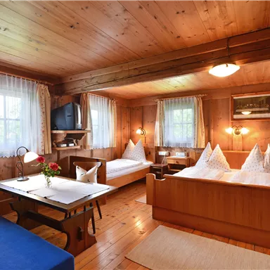 A cozy room with wooden paneling and two beds. There is a table, chairs, and large windows that let in plenty of light.