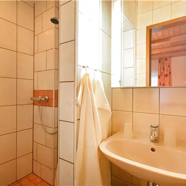 A modernly designed bathroom with a shower area and a sink. White tiled walls and a mirror create a bright ambiance.