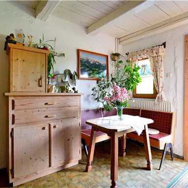A cozy room with a table, chairs, and a wooden dresser. Flowers in a vase add color and freshness to the decor.