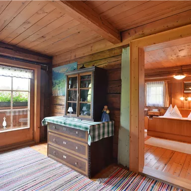 A cozy room with wooden walls and a wooden floor. In the foreground sits a chest of drawers and a windowsill with a view of nature.