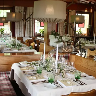 Ein stilvoll eingerichtetes Restaurant mit zwei gedeckten Tischen. Die Tische sind mit Blumen, Gläsern und Kerzen dekoriert, um eine gemütliche Atmosphäre zu schaffen.