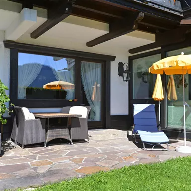 A cozy terrace with a table and two chairs. An umbrella and a lounge chair are ready to enjoy the sun.