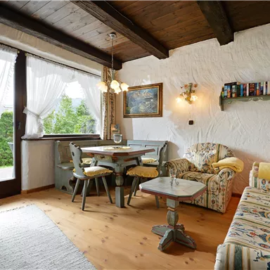 A bright living room with cozy furniture and a view of the garden. The room has large windows and a warm, inviting atmosphere.