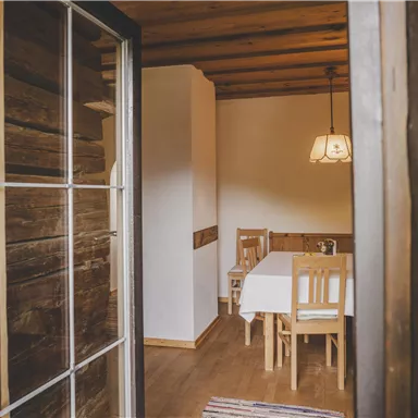 Ein einladender Raum mit Holzwänden und einem Tisch mit Stühlen. Licht strömt durch die Tür und schafft eine gemütliche Atmosphäre.
