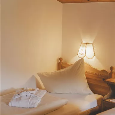 Ein gemütliches Schlafzimmer mit einem Holzbett und einem Kissen. An der Wand befindet sich eine sanfte Lichtquelle.