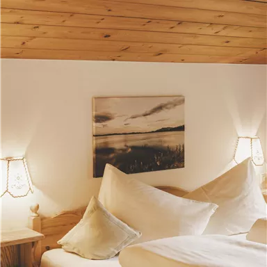 Ein gemütliches Schlafzimmer mit Holzdecken und einem großen Bett. Die Wände sind mit sanfter Beleuchtung und einem dekorativen Bild geschmückt.